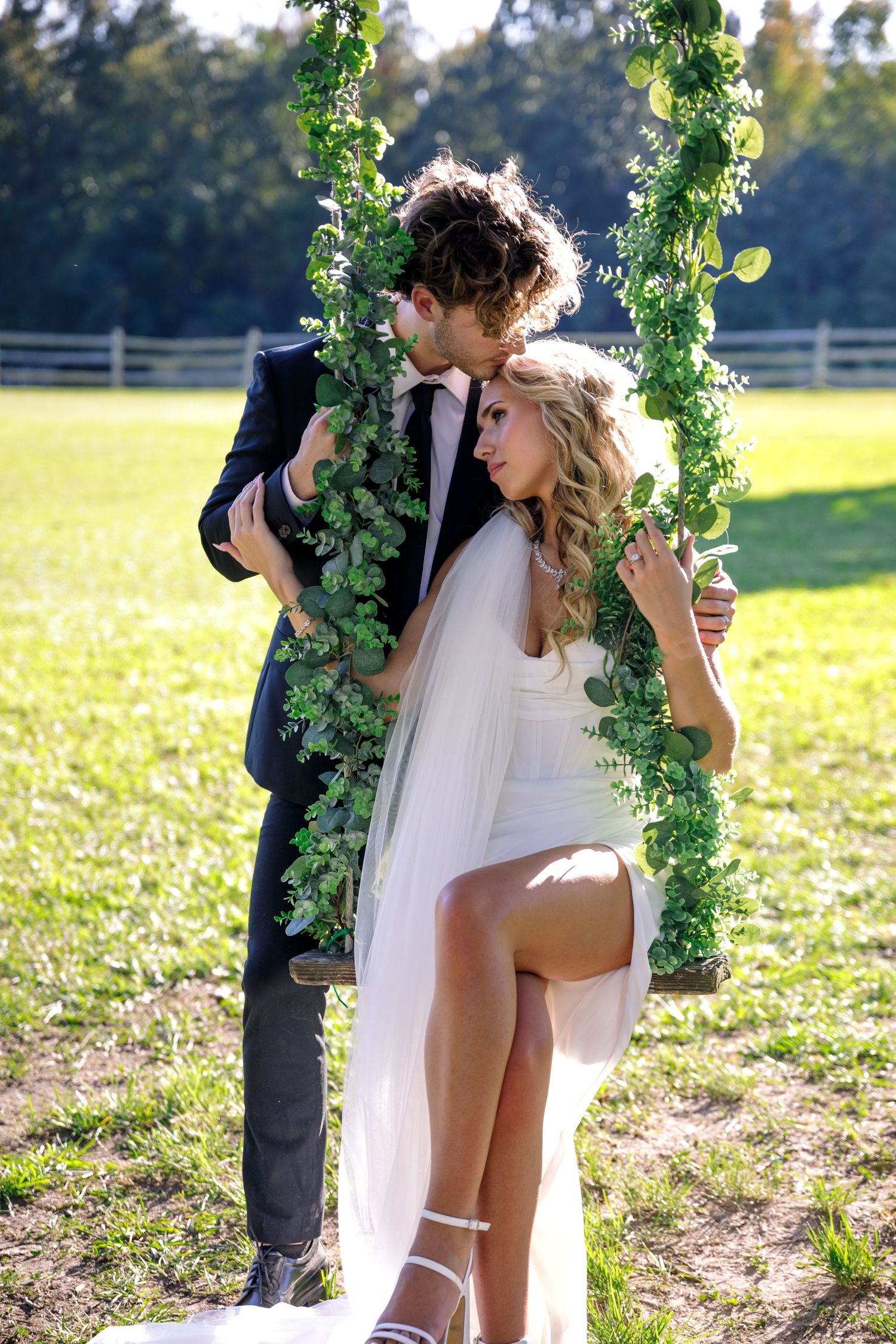 Wedding couple sharing a moment under a floral arch in a sunny meadow.