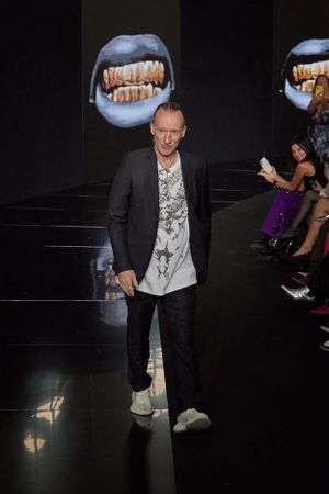 Fashion show runway with dramatic lighting featuring large mouth projections in background.