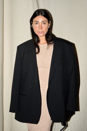 Model wearing an oversized black blazer over a beige dress against a light backdrop.