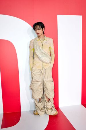 Model in beige cargo ensemble poses against geometric red and white backdrop.