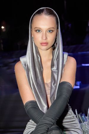 Model in silver hooded dress with long black gloves poses at nighttime fashion event.