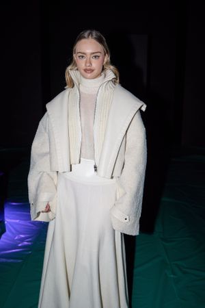 Model wearing cream-colored winter ensemble with turtleneck and oversized coat at fashion show.