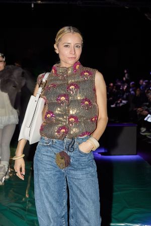 Fashion show guest wearing floral embroidered vest with jeans and white handbag.