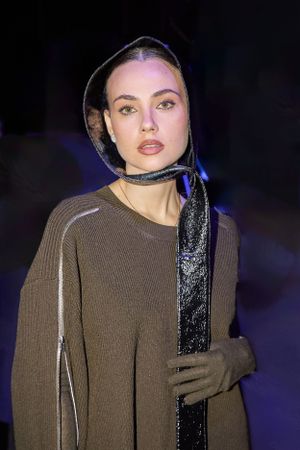Model in brown sweater and sparkly black headscarf at nighttime fashion event.