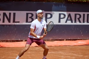Tennis player in white shirt prepares return shot on clay court during BNP Paribas tournament.