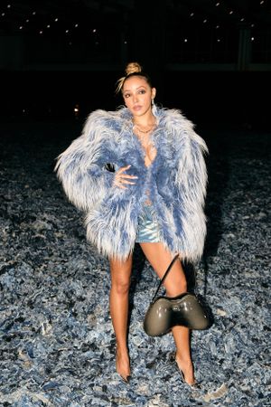 Glamorous light blue furry coat styled with shorts and handbag against dark background.
