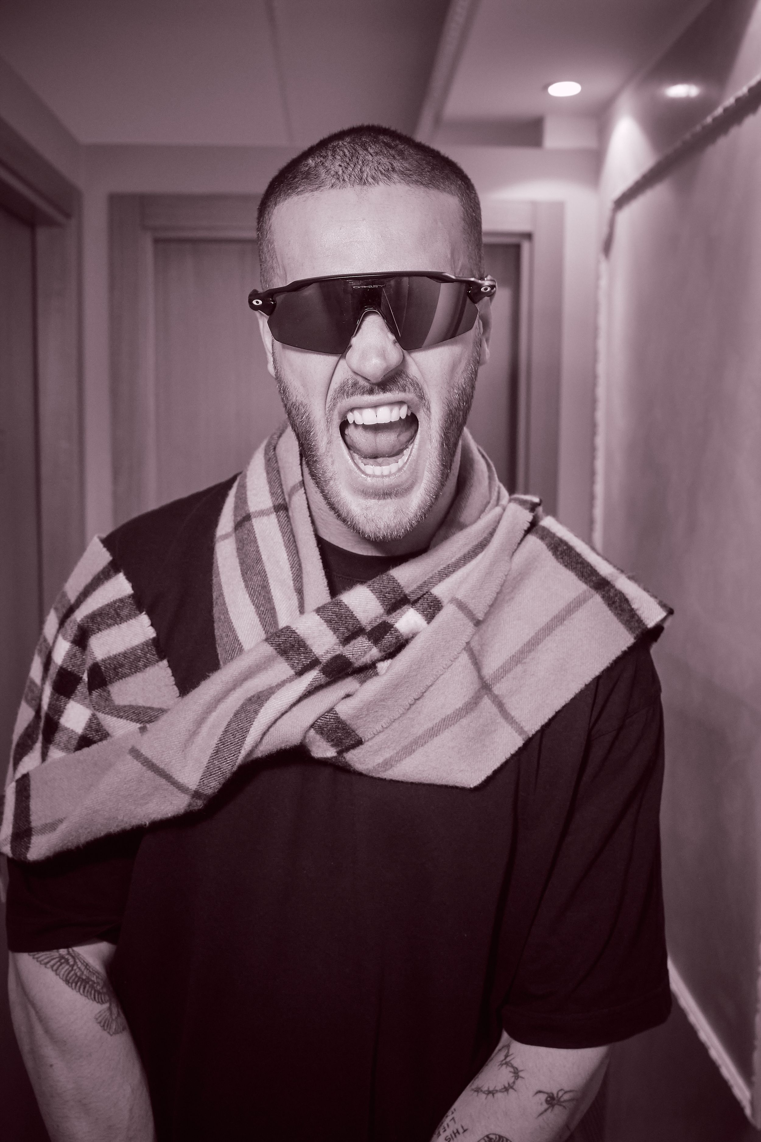 Excited performer in sunglasses and striped scarf laughs in hallway.