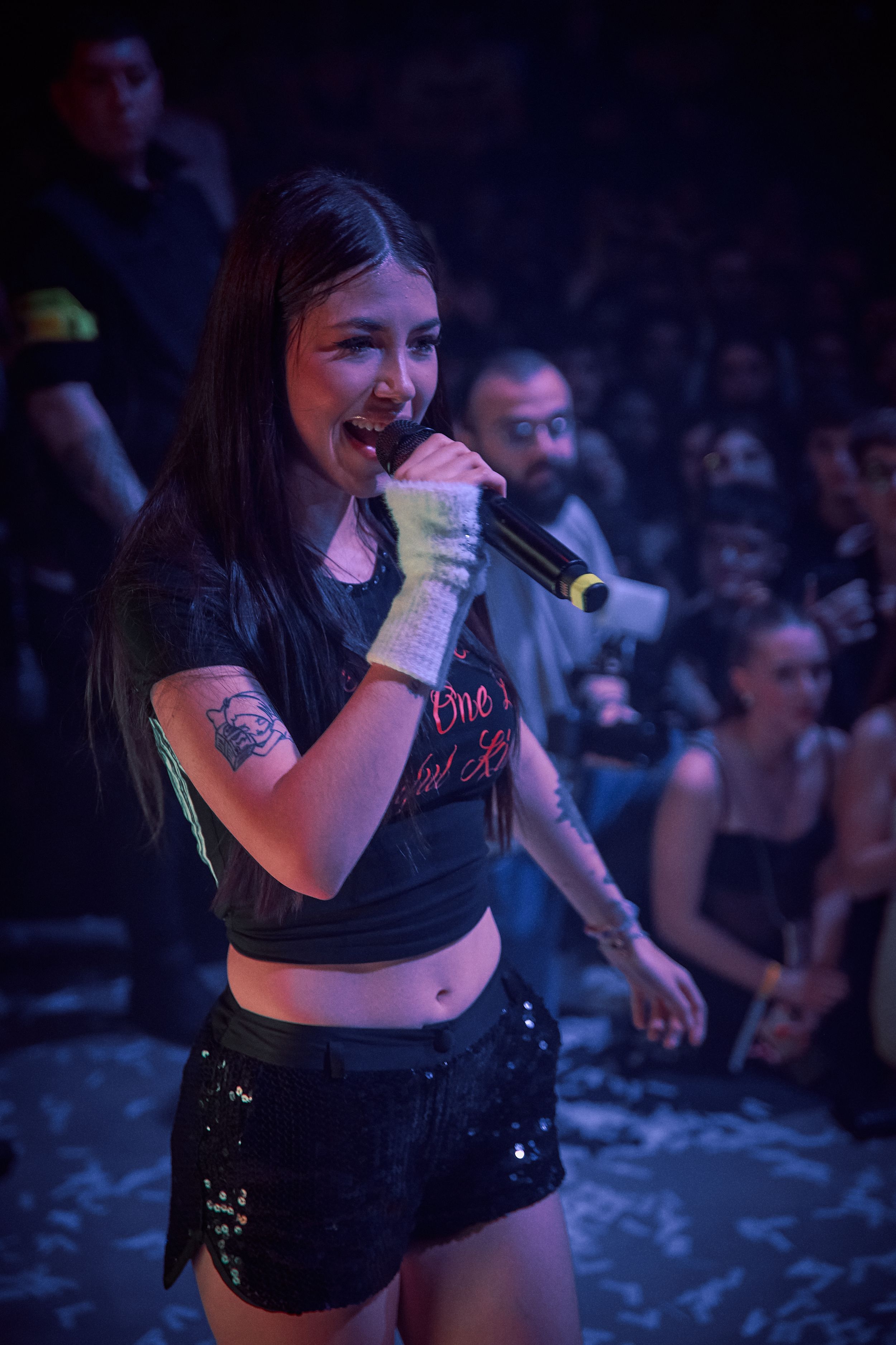 Concert performer in black outfit enthusiastically sings during live show.