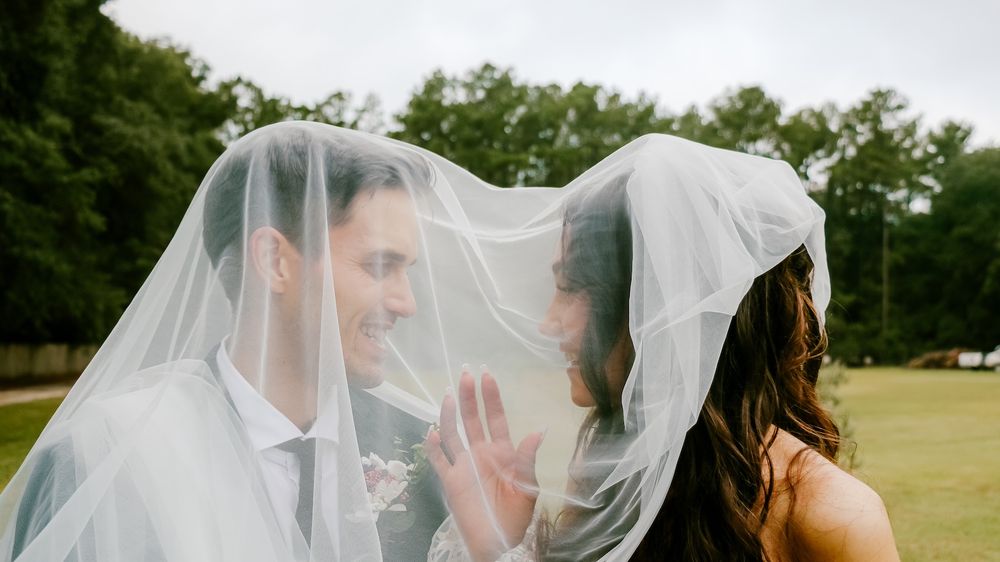 Playful wedding moment under a flowing veil outdoors.