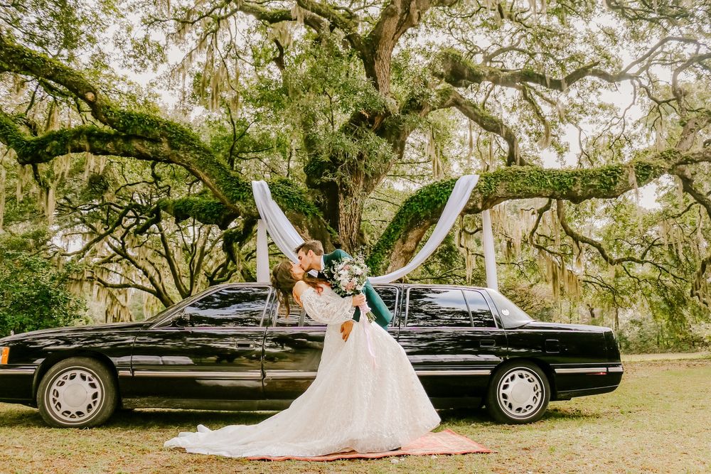 Wedding couple celebrating next to vintage black car under Spanish moss covered trees.