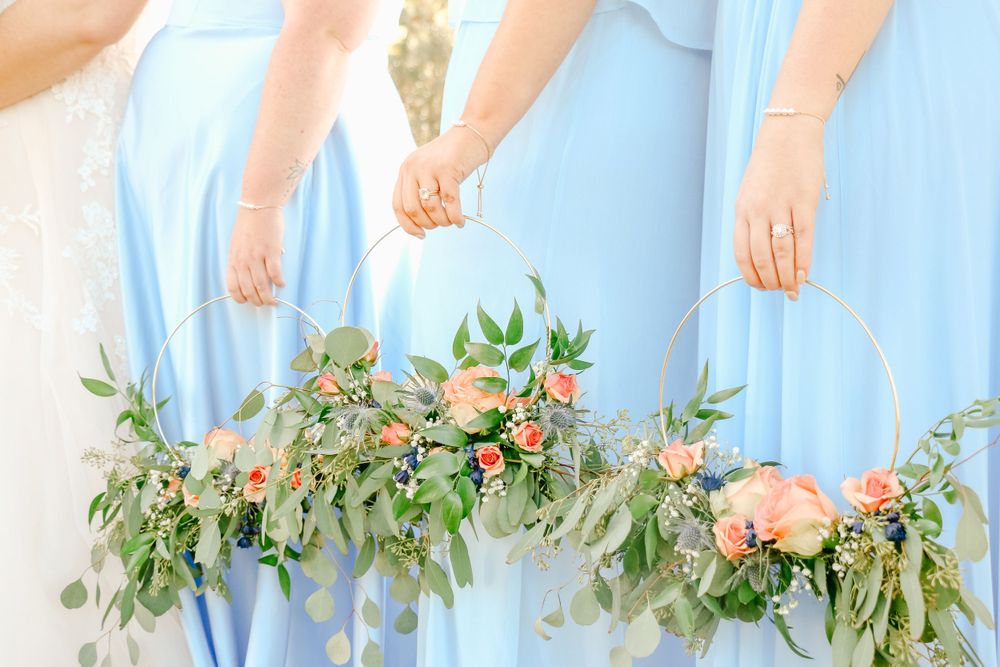 Bridesmaids in light blue dresses holding floral bouquets with peach roses and greenery.
