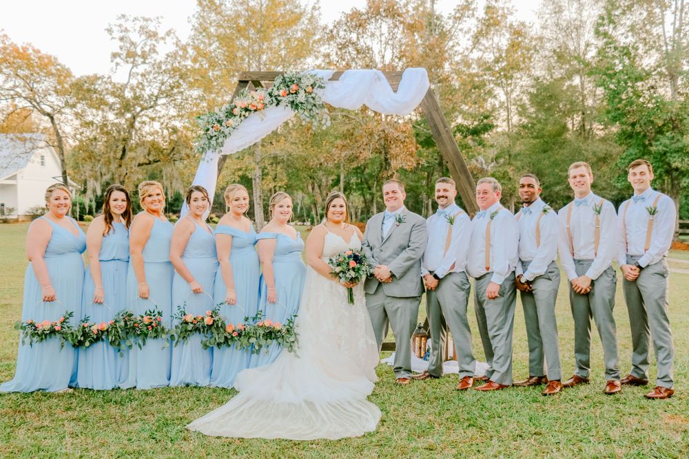 Wedding party in light blue dresses and gray suits poses outdoors under autumn trees.