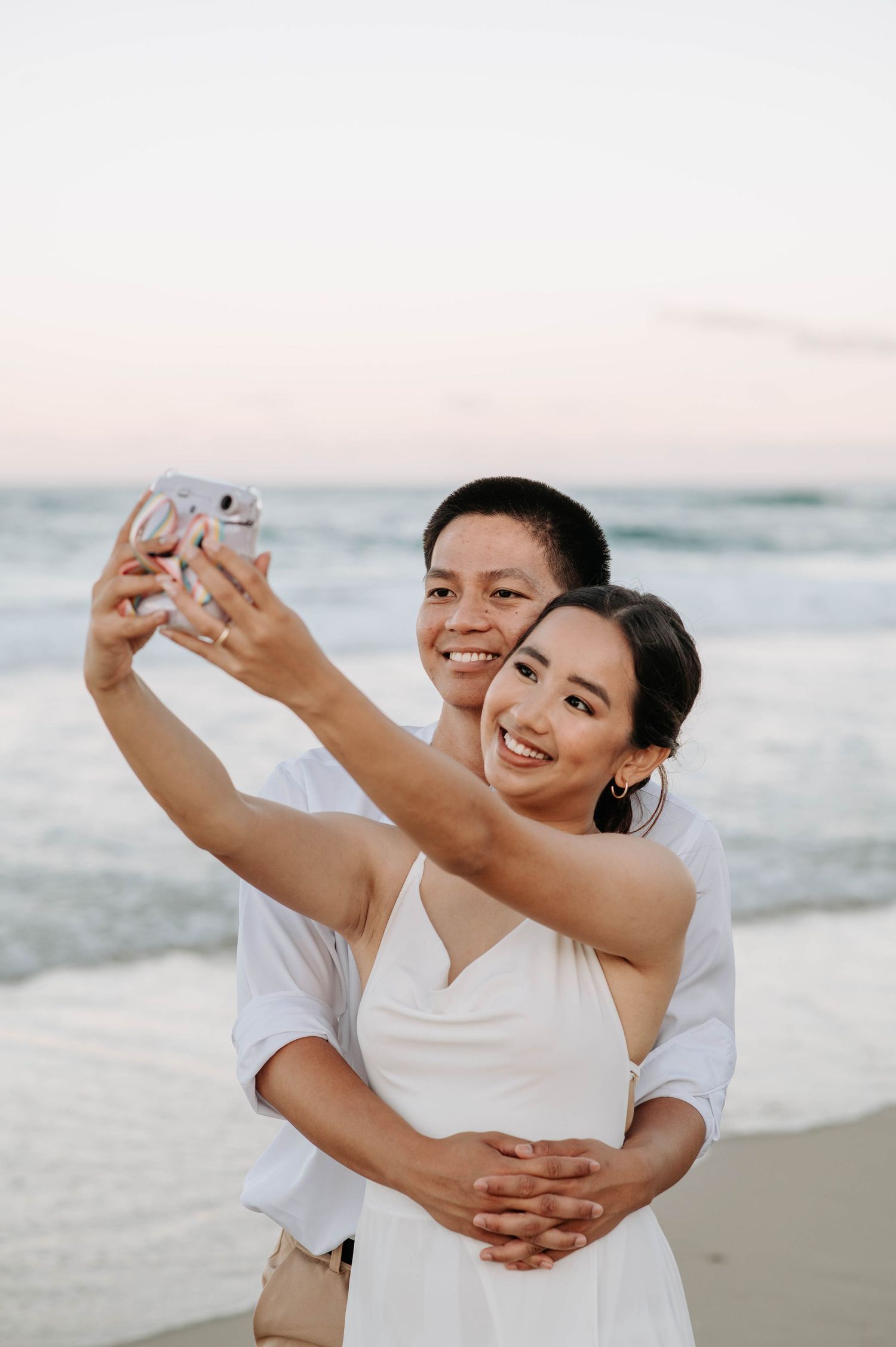 A couple taking a selfie together on the beach at sunset.