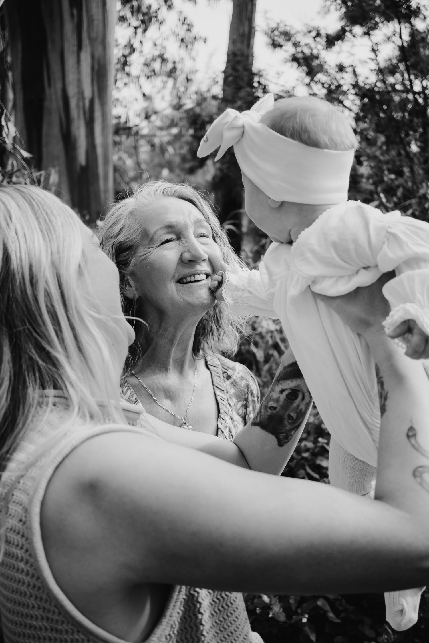 Mum holding her baby that is touching her grandmothers face.