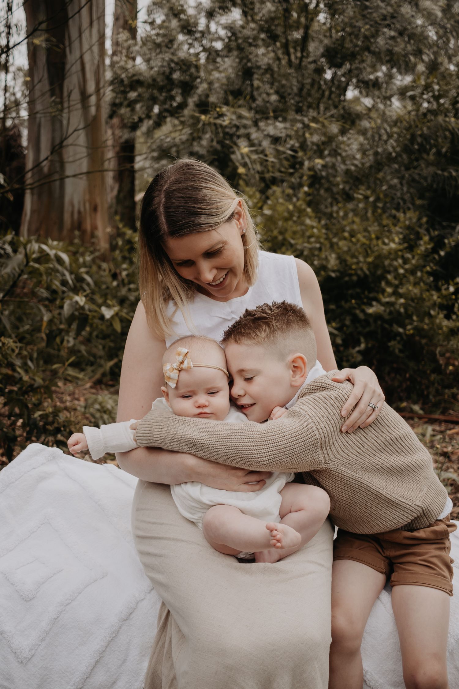 Mum holding baby while getting a hug from her son.