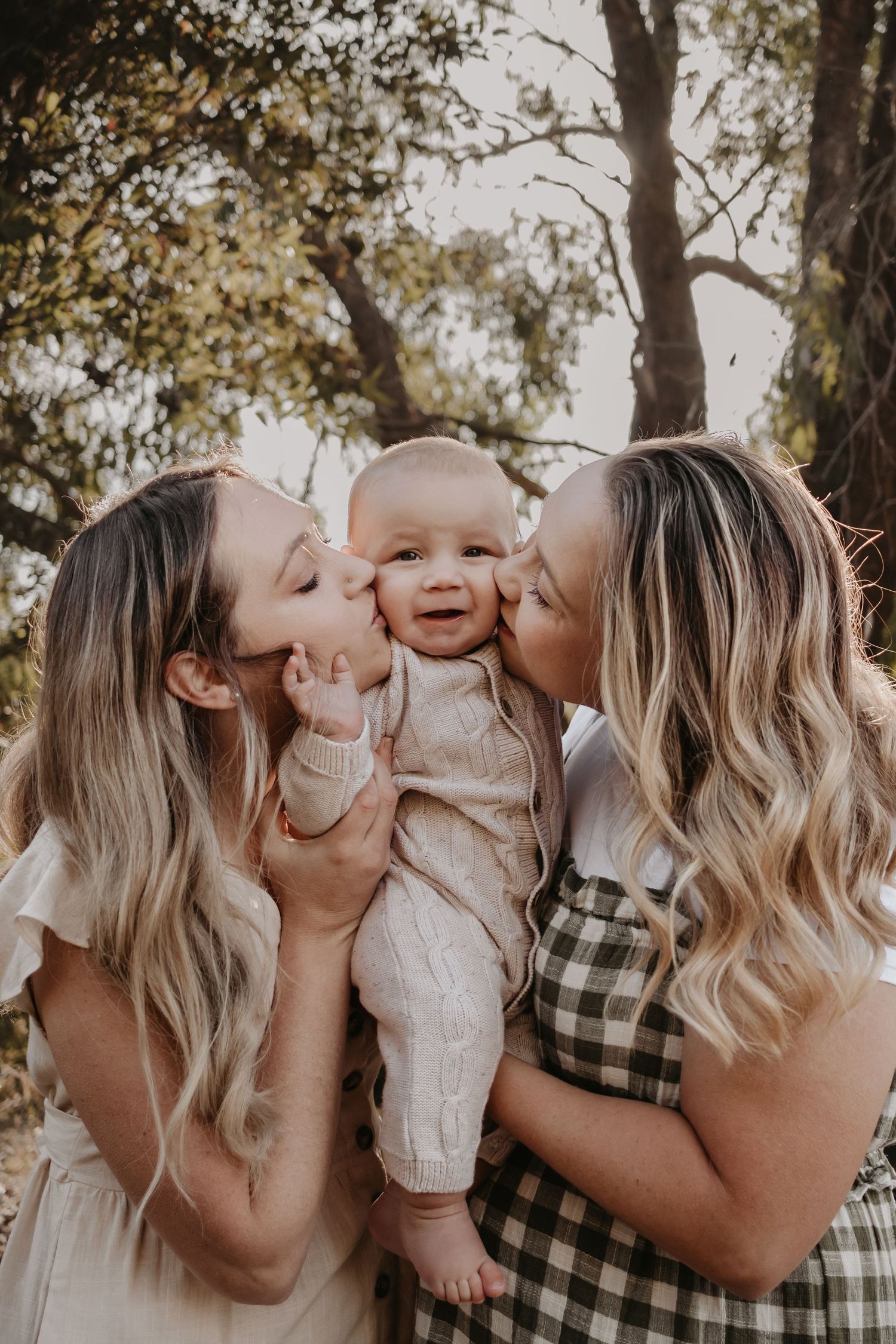Mum and sister kissing either side of baby's cheeks.