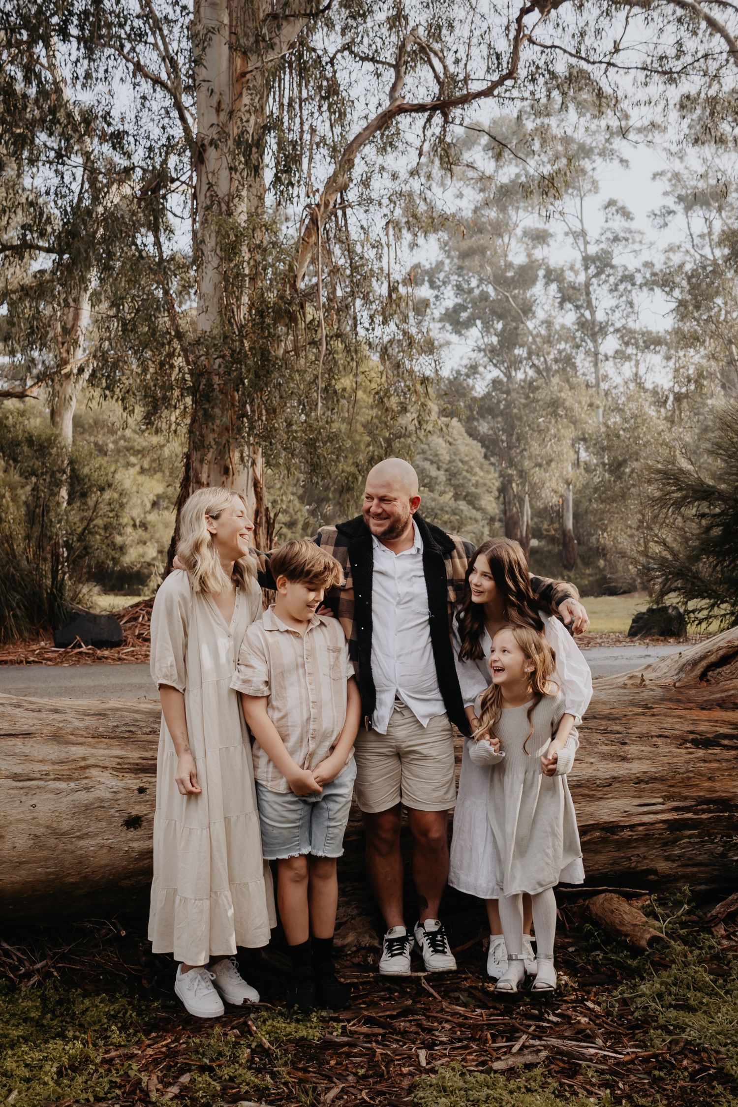 Family leaning against a log all hugging and looking at each other.