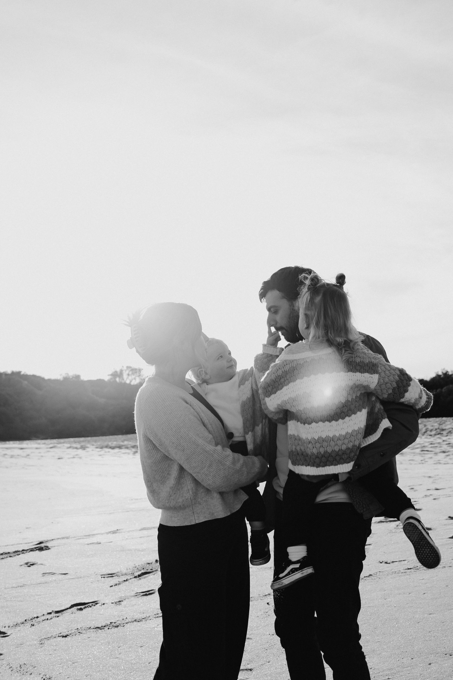 Family standing together at the beach while daughter touches dad's nose.
