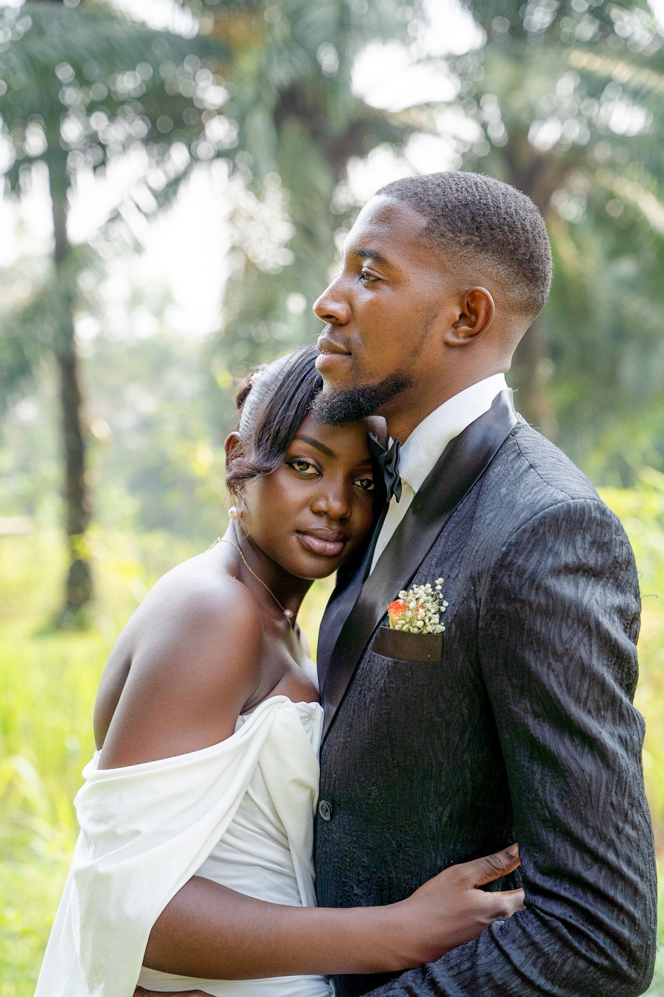 A romantic wedding portrait shows a couple embracing outdoors with soft natural lighting and greenery in the background.