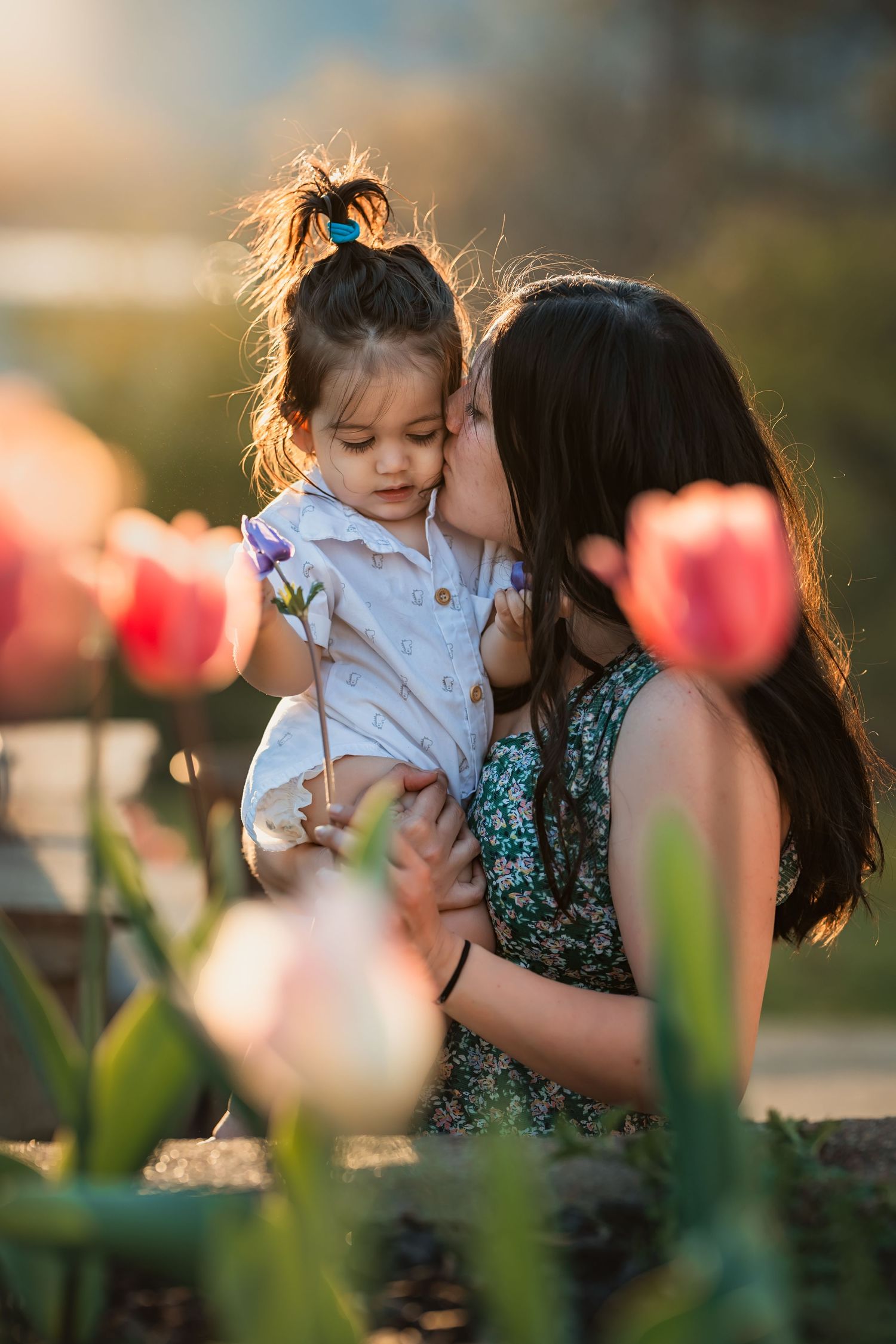 mother kisses her 18mo son at sunset behind some tulips