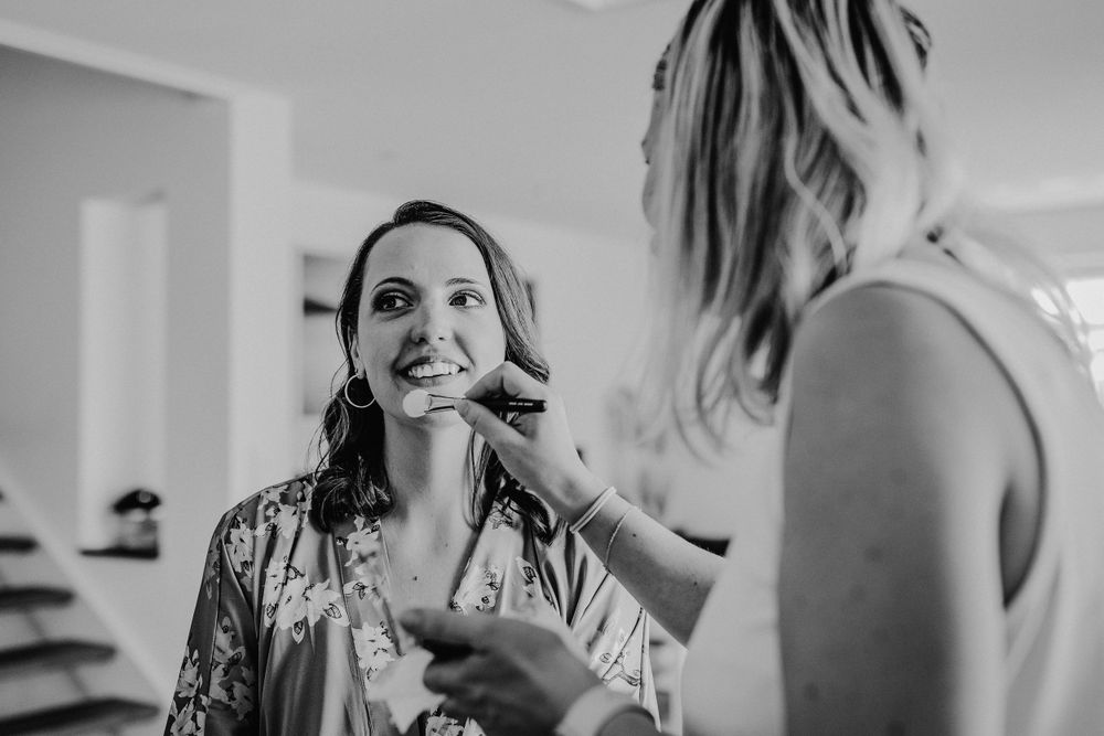 Black and white photo of bride having makeup applied while getting ready for wedding ceremony.