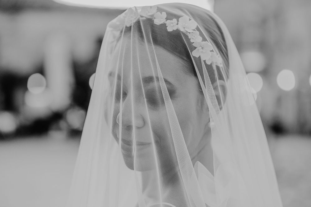 A delicate lace-trimmed bridal veil drapes over a figure in this dreamy black and white photograph.