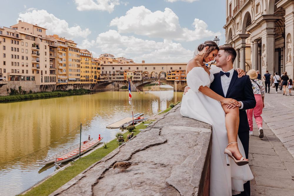 Romantic couple sitting along the historic Arno river in Florence with Ponte Vecchio bridge in background.