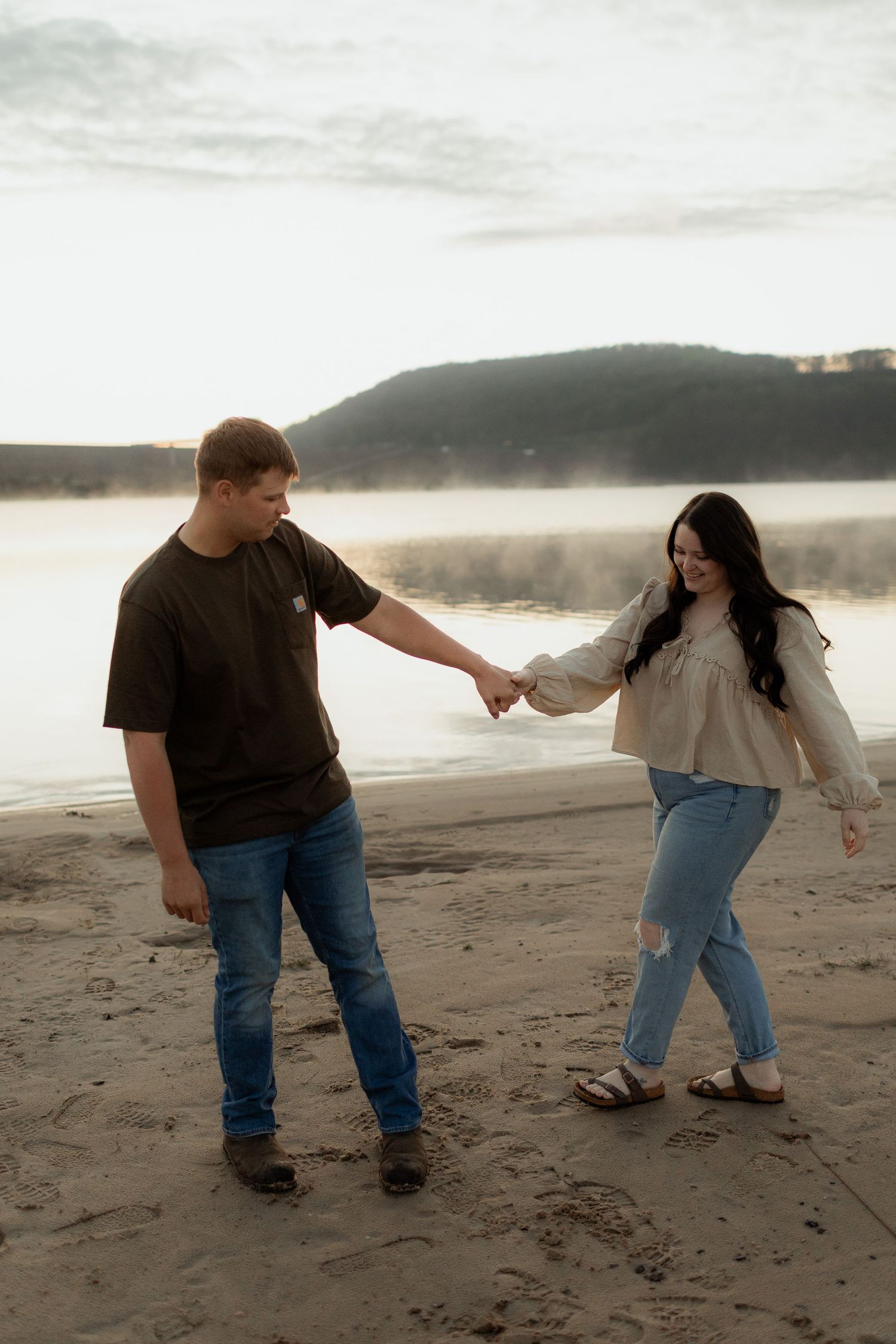 Couple sharing romantic moment by lake at sunset in casual outdoor setting.