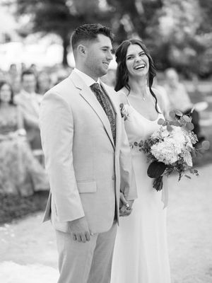 A joyful couple in wedding attire share a candid moment outdoors in black and white photography.