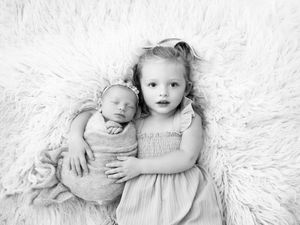 Black and white portrait of baby lying on soft white blanket in gentle lighting.