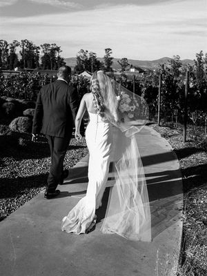 Black and white photo of a couple walking through a vineyard on their wedding day.
