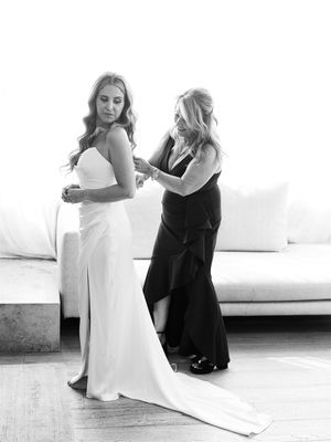 Black and white photo of a wedding dress fitting with two people in an elegant room with white furniture.