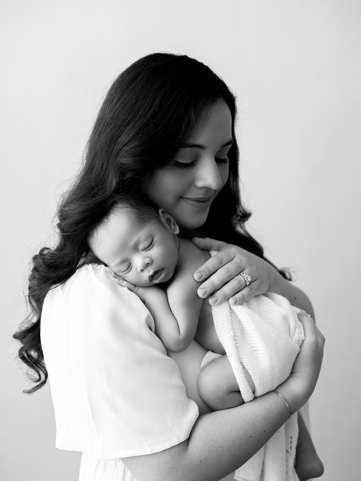 A series of four black and white photos showing tender moments between a mother and baby in matching white outfits.
