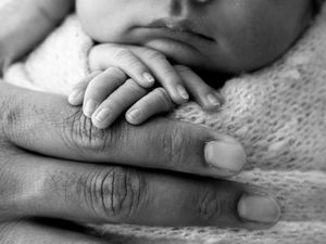 Close-up black and white photo of hands gently touching and intertwined on a textured surface.