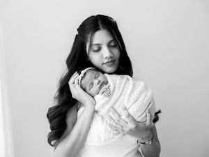 A tender black and white portrait of a mother cradling her sleeping newborn baby against her chest.