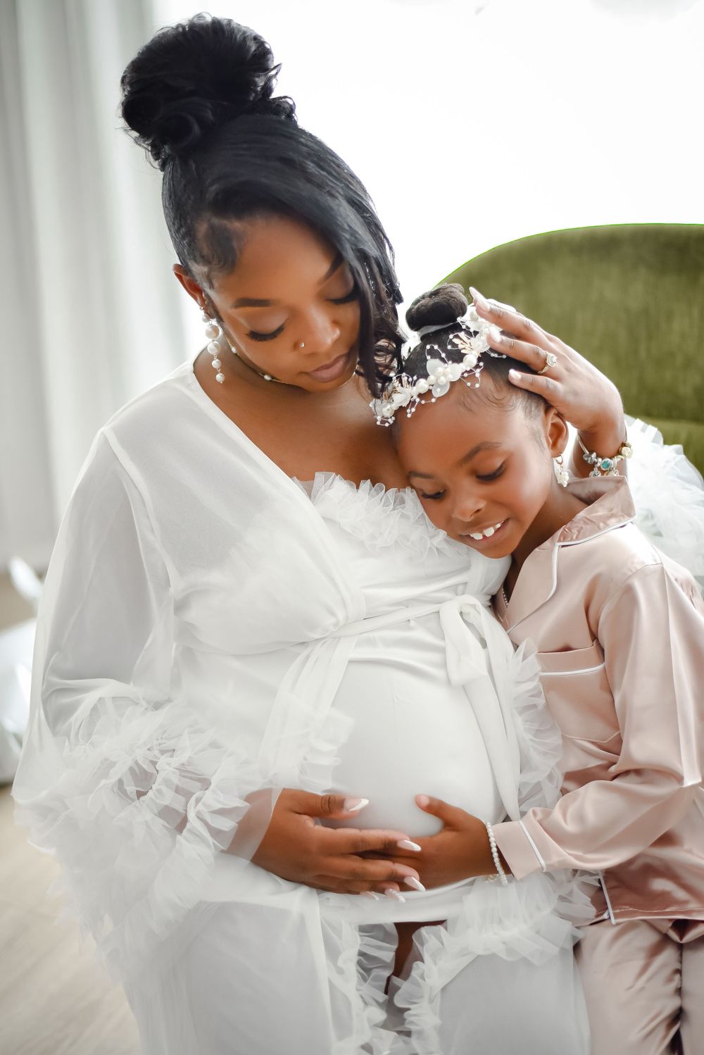 An intimate maternity moment captured in a bright indoor setting with soft white decor.