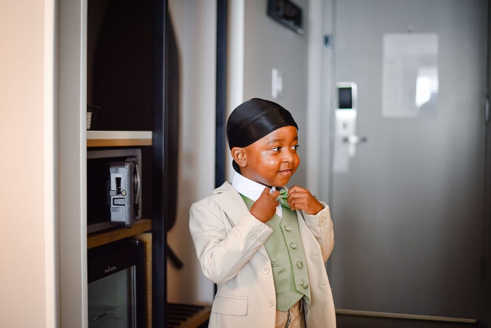 Small figure wearing a light colored blazer and green shirt in a modern interior space.
