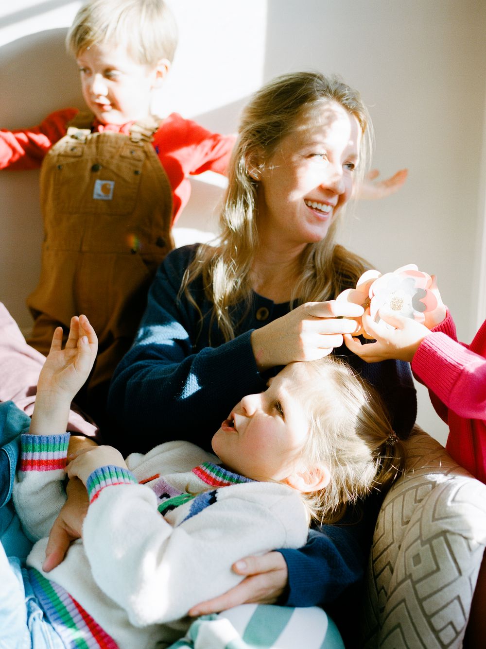 A joyful woman laughs with three young children in colorful clothes, playing together in warm natural light.