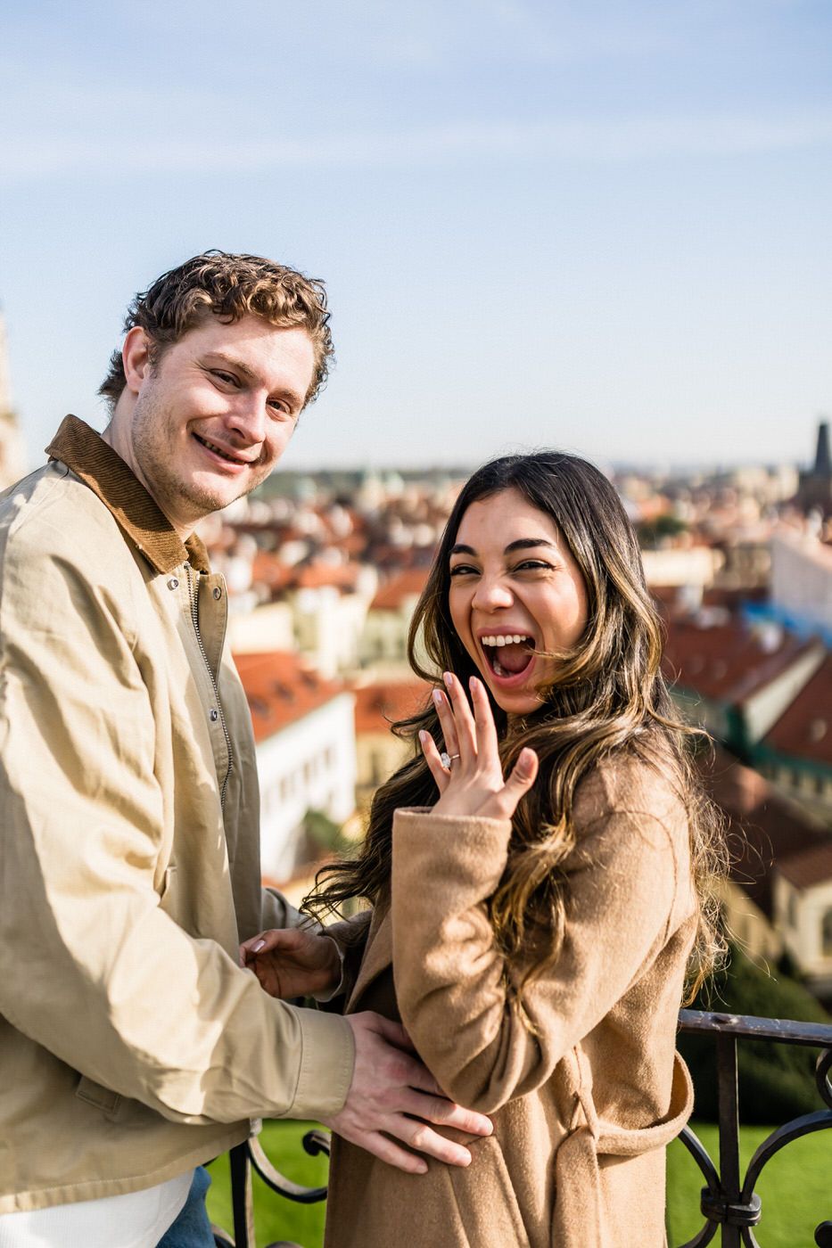 Two people share a joyful moment together on a sunny day with city rooftops in the background.