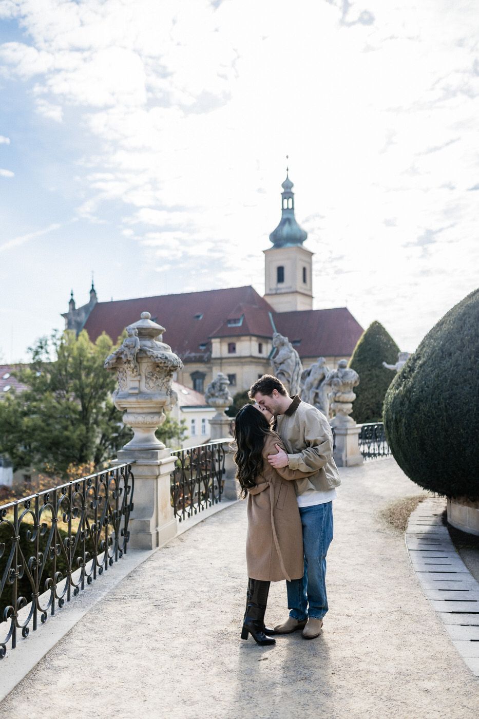 A romantic moment captured on a baroque terrace with ornate railings and a historic church building in Prague.