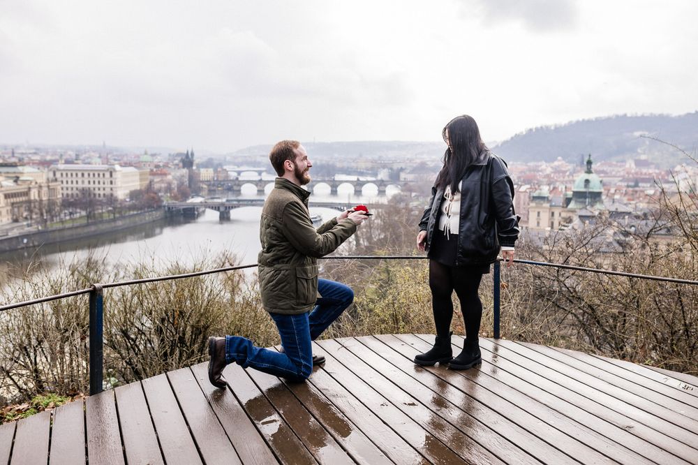 A romantic proposal moment on a wooden viewing deck overlooking the city of Budapest and Danube River on a cloudy day.