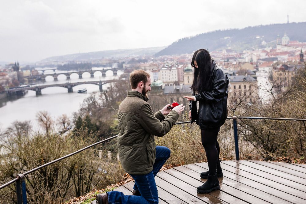 Couple sharing a romantic moment at a scenic overlook with city views and bridges in the background.
