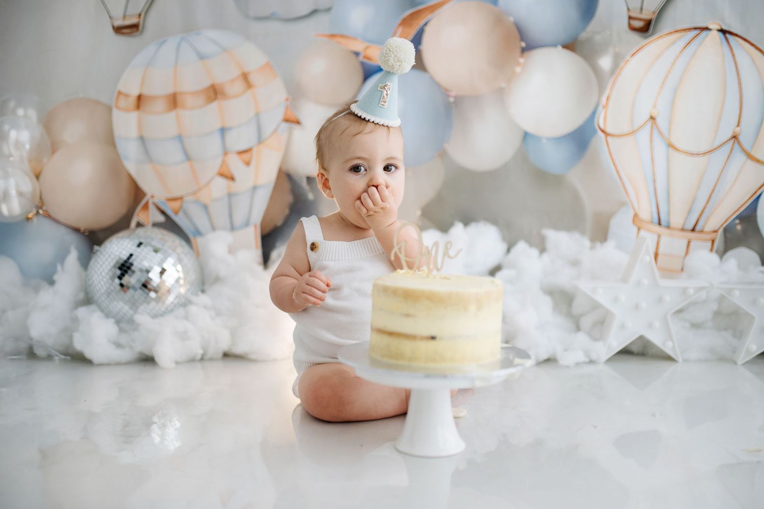 Baby portrait with hot air balloon themed backdrop and plush teddy bear.
