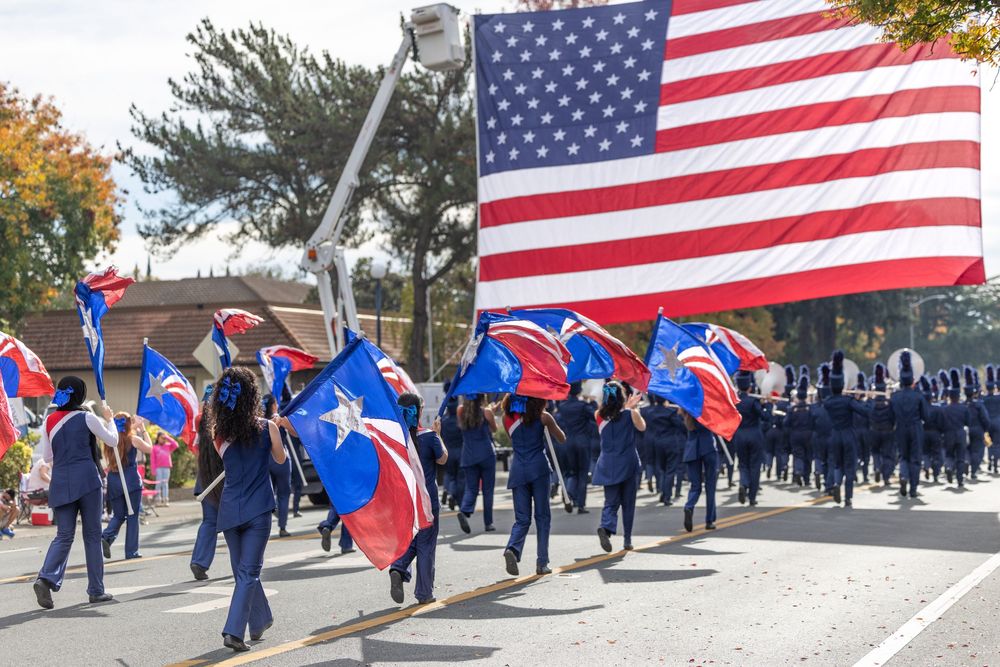 Marchers carry American and Puerto Rican flags during a parade on a sunny autumn day.