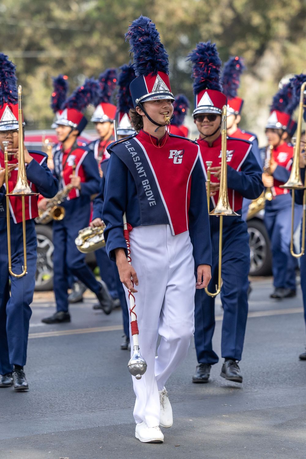 Marching band members in red and navy uniforms perform while walking in formation during a parade.