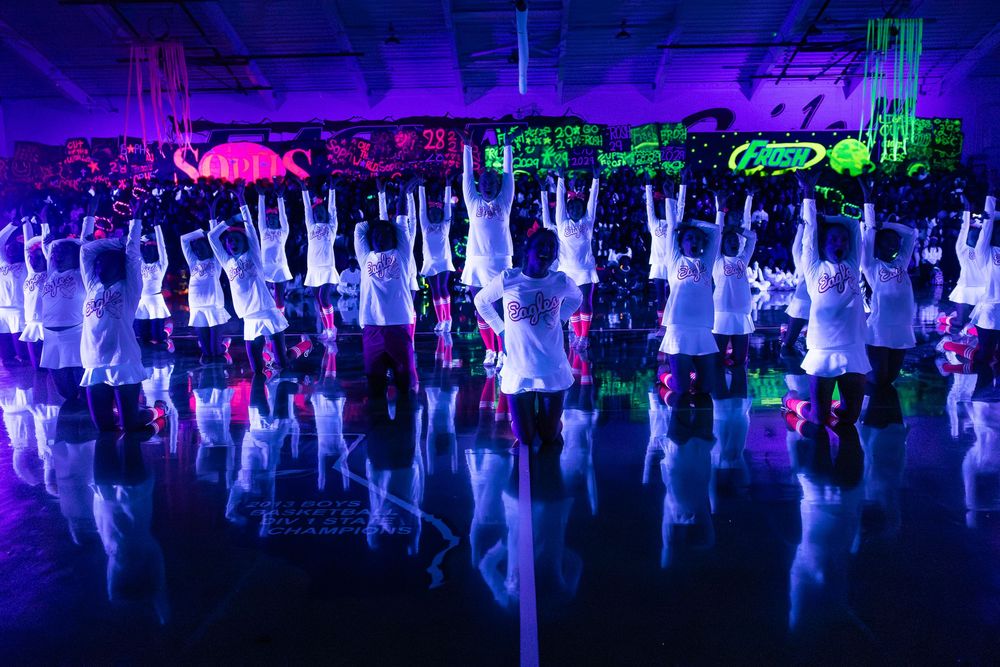 Colorful nightclub scene with purple and blue lighting illuminating a crowded dance floor filled with party-goers.