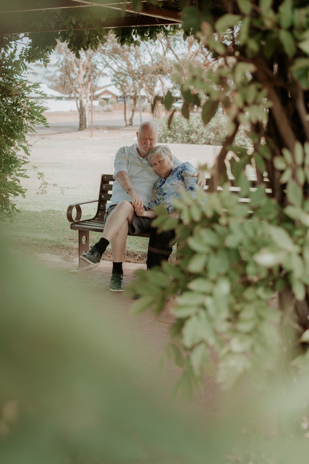Elderly couple sharing an intimate moment while sitting together on a park bench in nature.