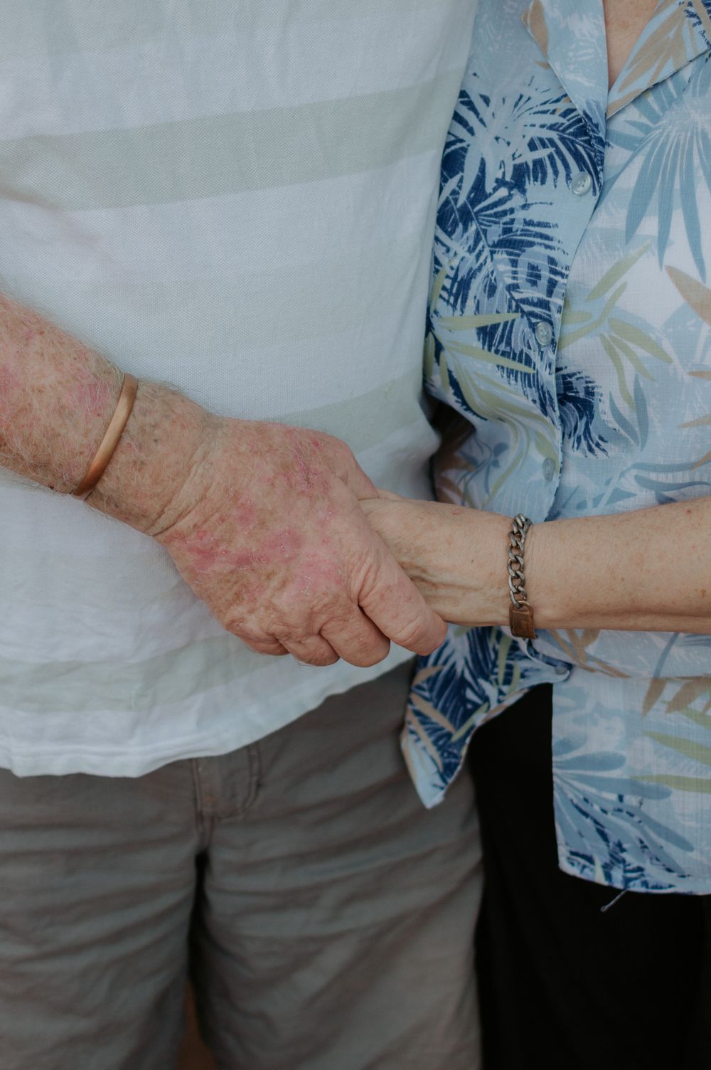 Close-up shot of two hands clasped together with one wearing a bracelet against floral clothing.