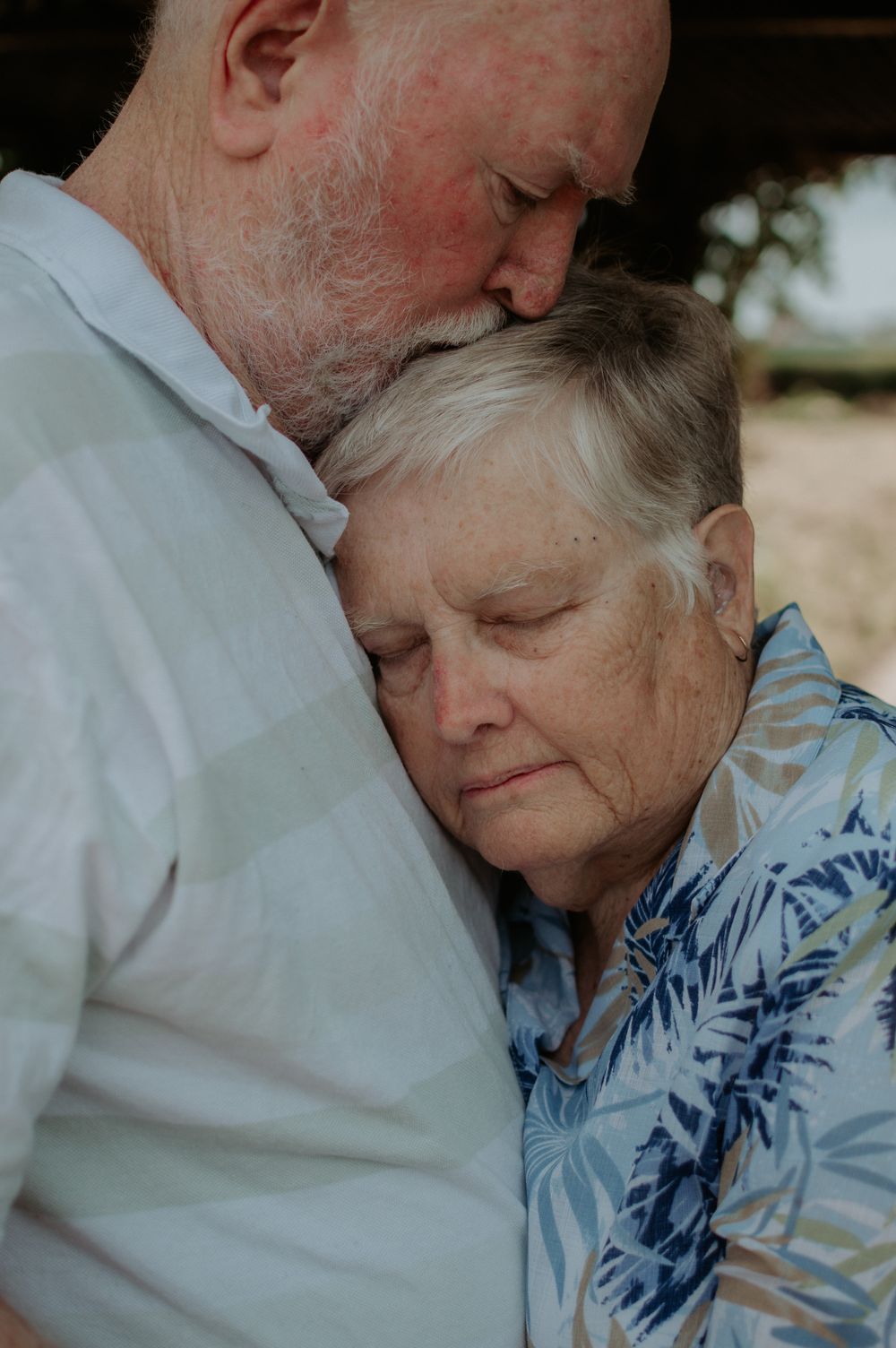 Intimate moment between elderly couple with woman in floral shirt resting against partner.
