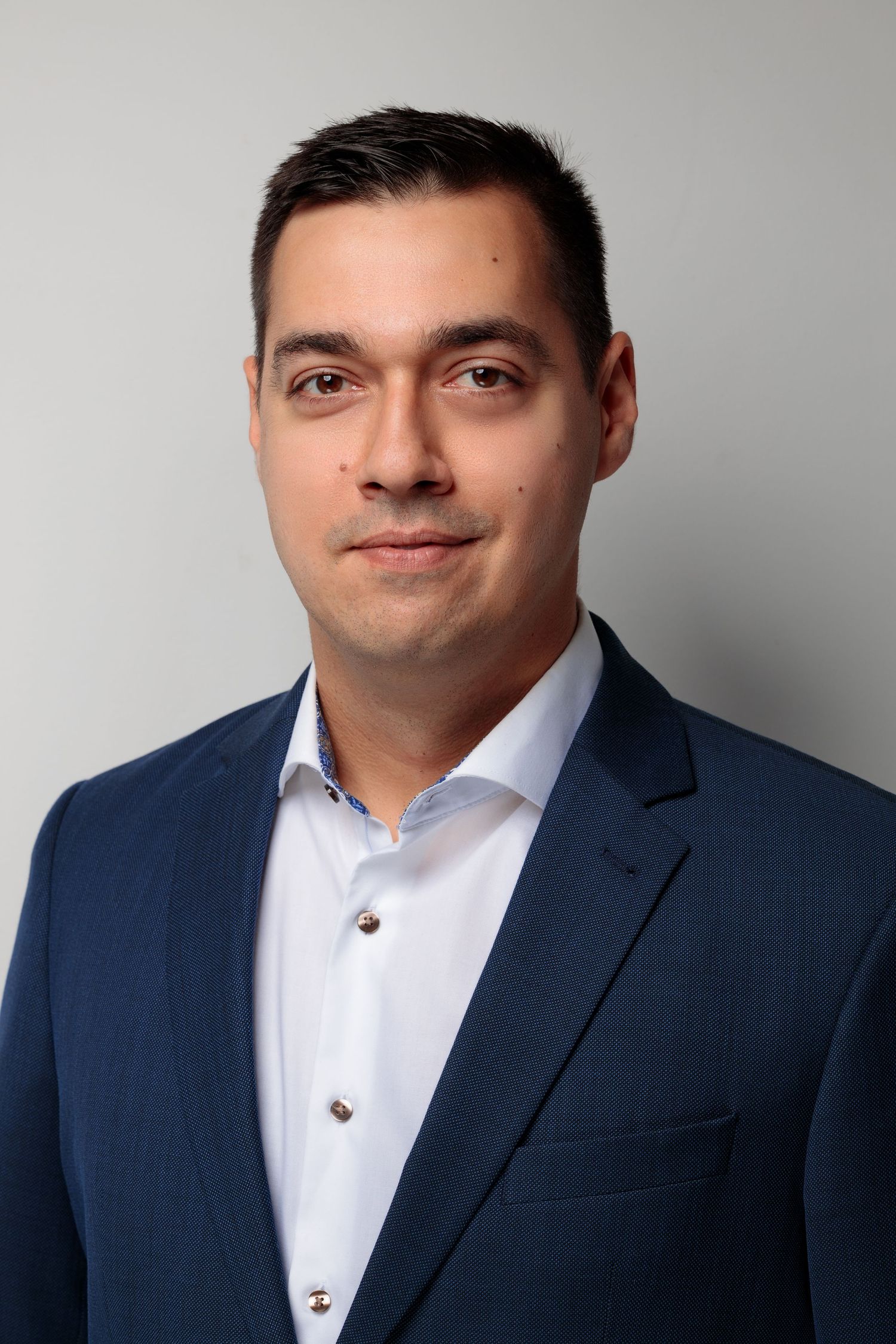 Business portrait of man in navy suit jacket and white shirt against grey backdrop.